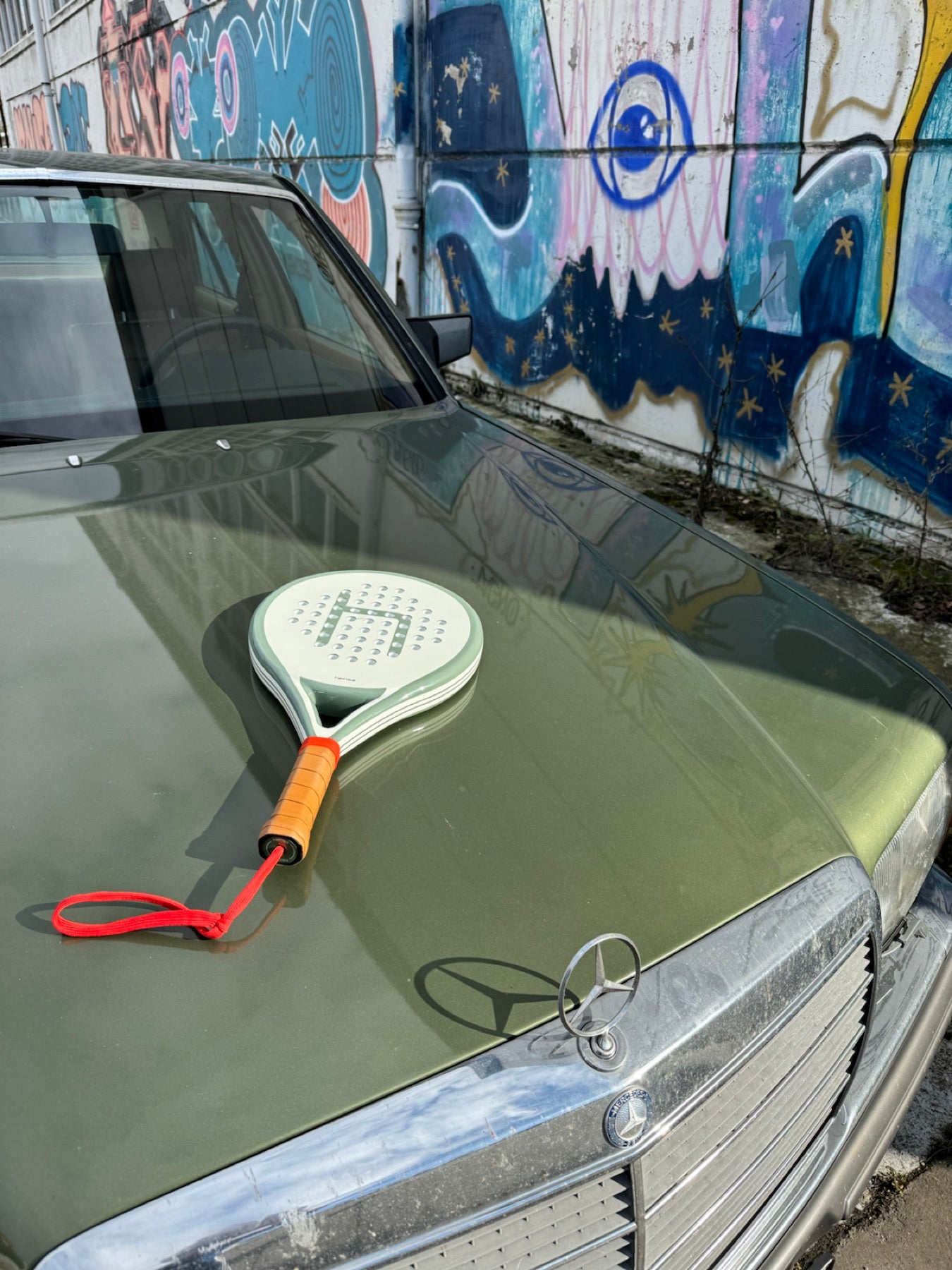 heinsa padel schläger auf einem klassischen auto vor urbaner kunst